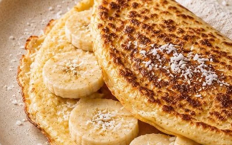 Une crêpe KetoZen dorée, pliée en deux sur des tranches de banane, dans une assiette