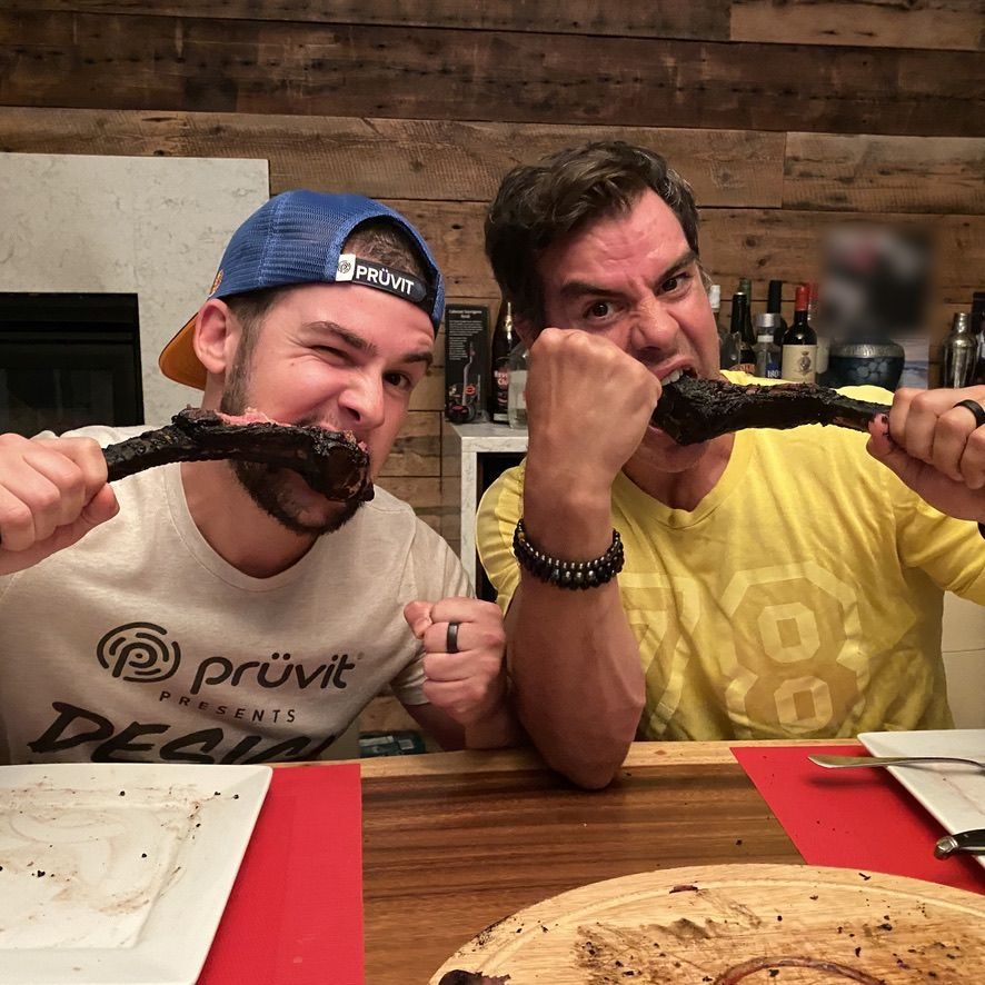 Mick et Yann à table, chacun mord dans un tomahawk tenu par l'os