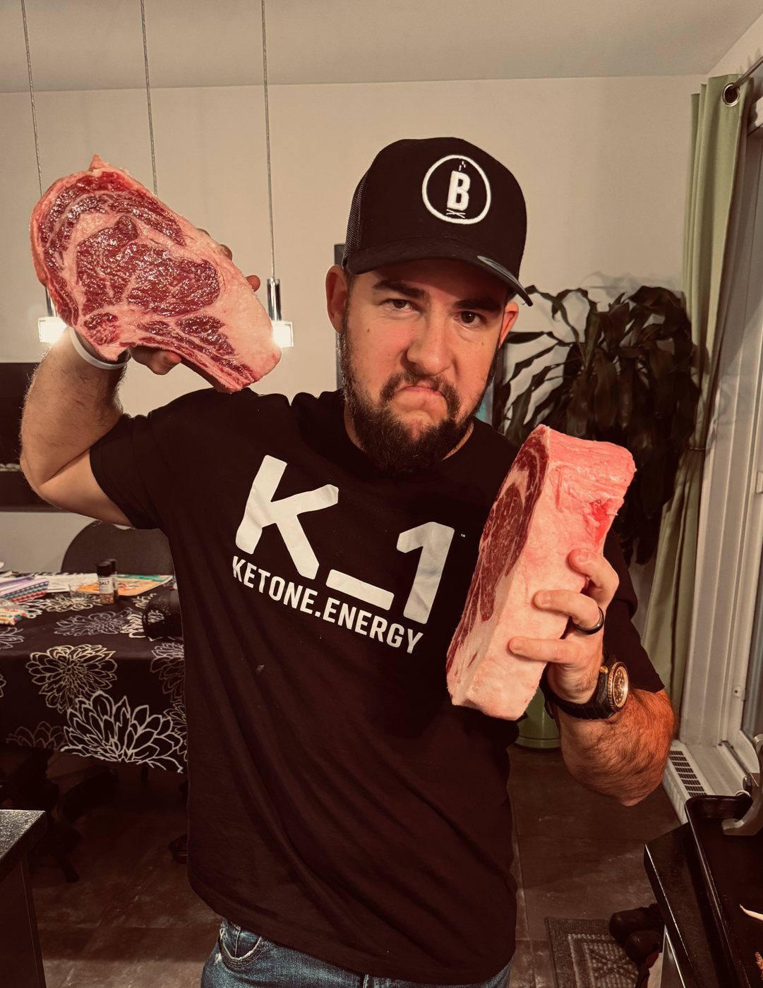 Mick, casquette et chandail K1, brandit deux grosses pièces de bœuf crues